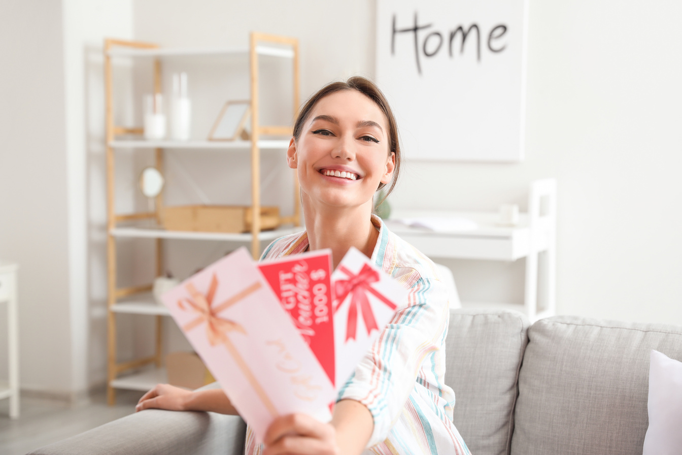Beautiful Young Woman with Gift Cards at Home